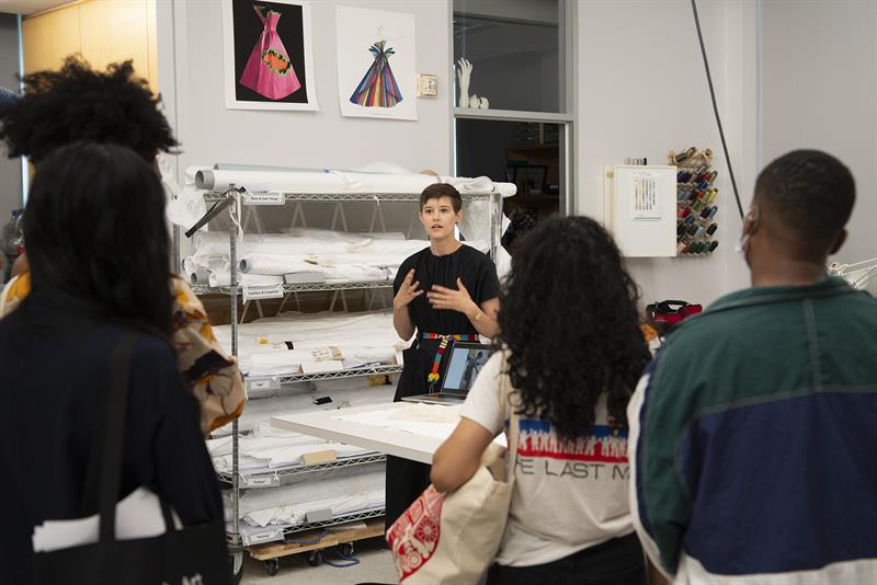 A student is standing in front of a rack of rolled textiles, speaking to a group visitors inside the conservation lab.