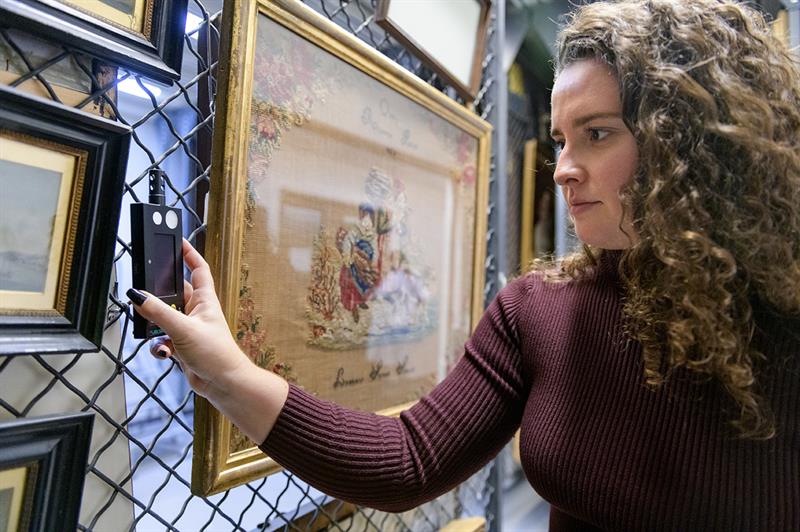 A student holds light meter close to the surface of a painting.