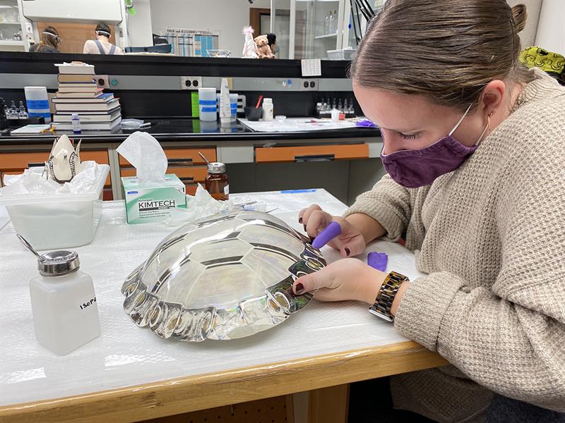 A student runs her gloved finger across the edge of a layer of epoxy.