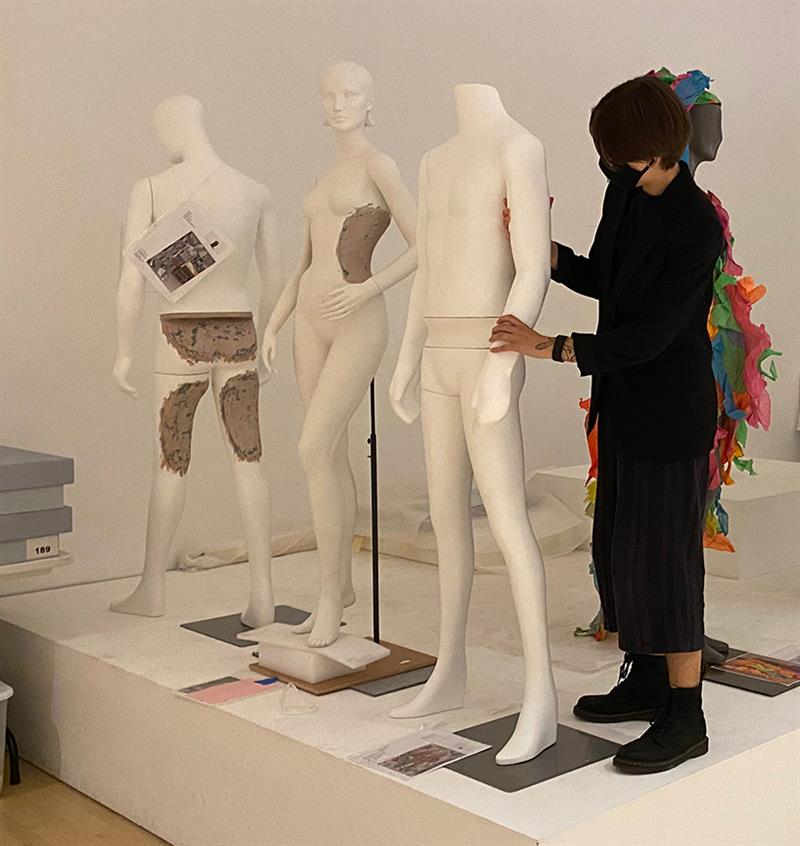 A student, wearing a mask, positions mannequins on a platform.