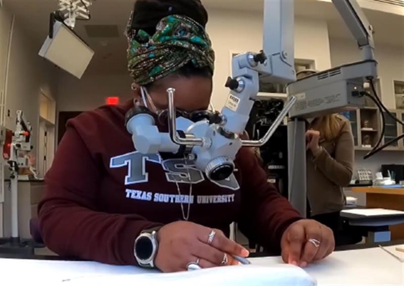 A student uses a microscope to examine a work on paper.
