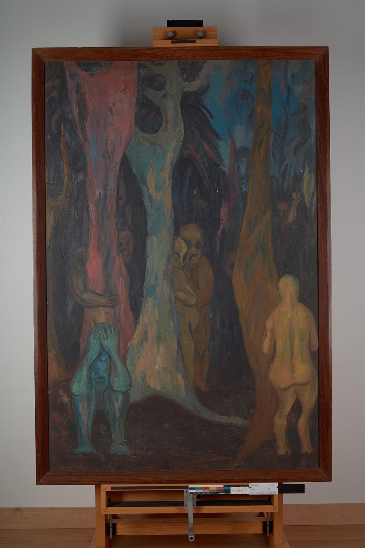 A multicolored painting of figures and trees. The painting is framed and sitting in an artist's easel.