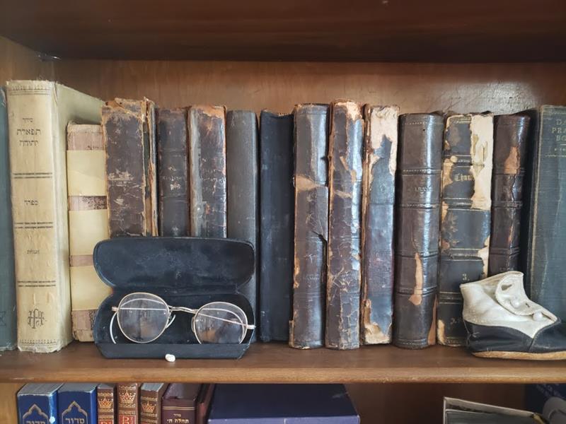 A image of a bookshelf with many old books, a pair of antique glasses, and a child's shoe.