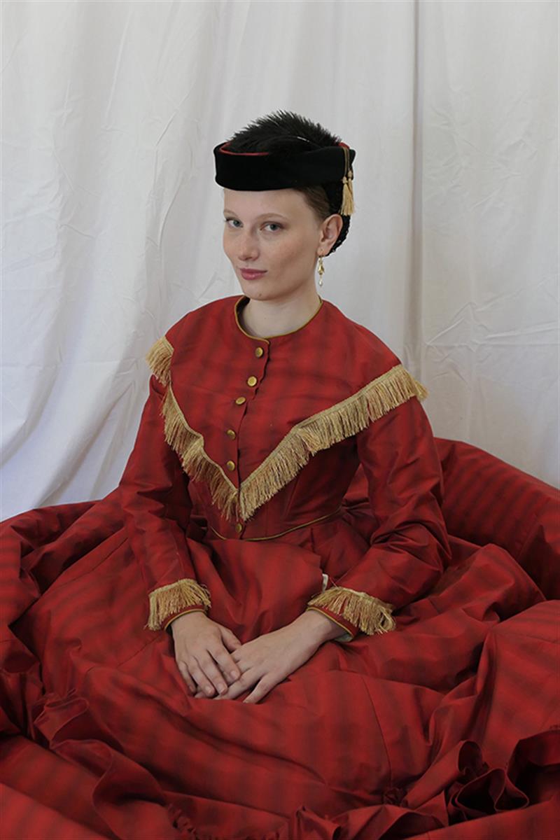 A student poses in a reprduction Victorian gown in red fabric with gold fringe.