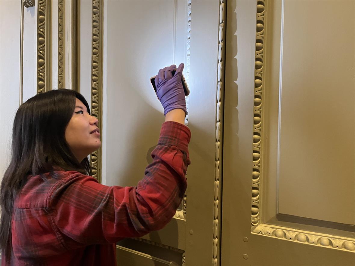 A student uses a flashlight to look at details in wooden carving on a door.