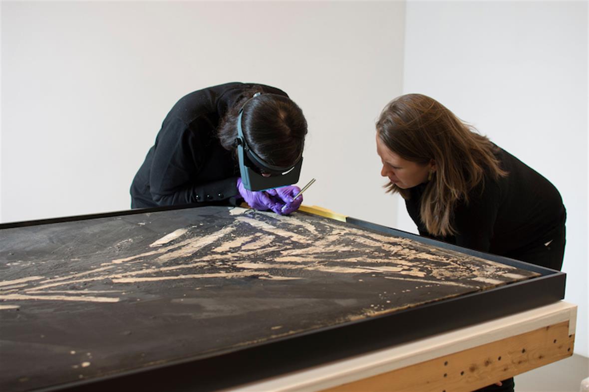A student and teacher examine a painting laid across a table.