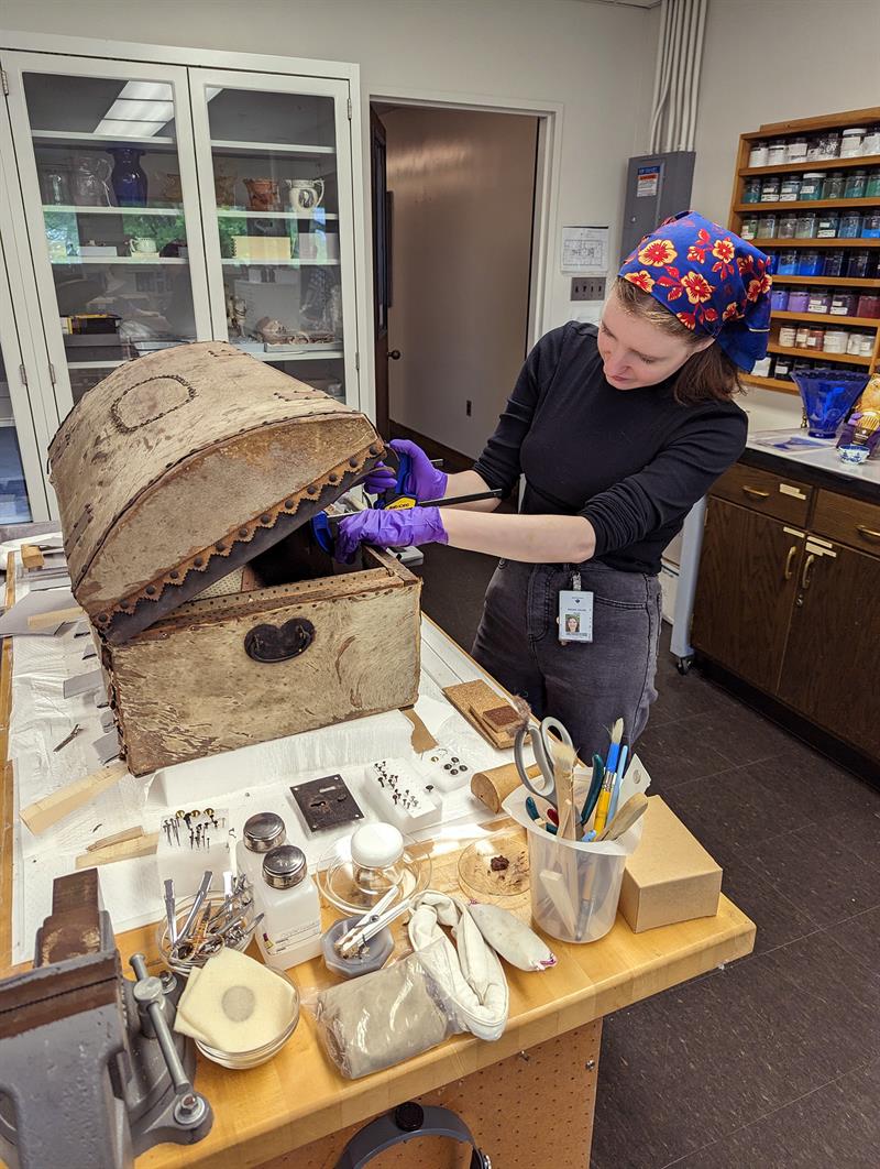 A student looks into the open trunk, which sits on a table next to conservation tools and materials.