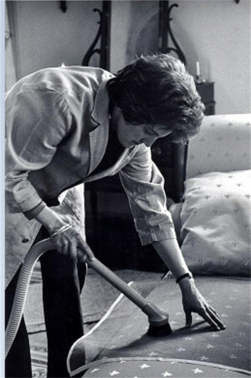 A conservator in a lab coat uses a vacuum brush and netting to clean the surface of upholstered furniture.