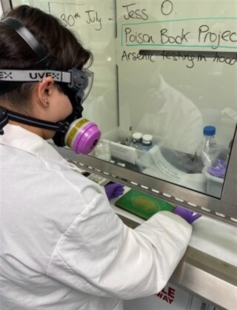 A student wearing a respirator works with chemicals under a fume hood.