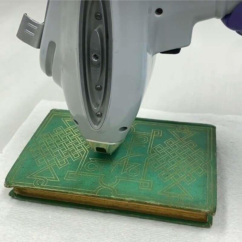 Portable analysis equipment is held close to the green cover of an old book.