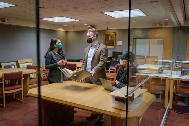 Students and a professor stand around a table in the Special Collections Library, looking at a book sitting on a book cradle.