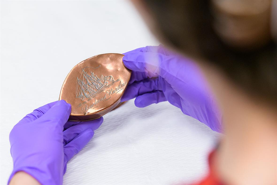 A student holds an oval-shaped copper-colored box in her gloved hands.