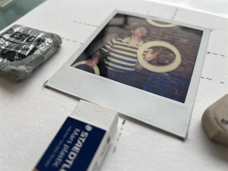 A polaroid picture sits on a table next to several types of eraser.