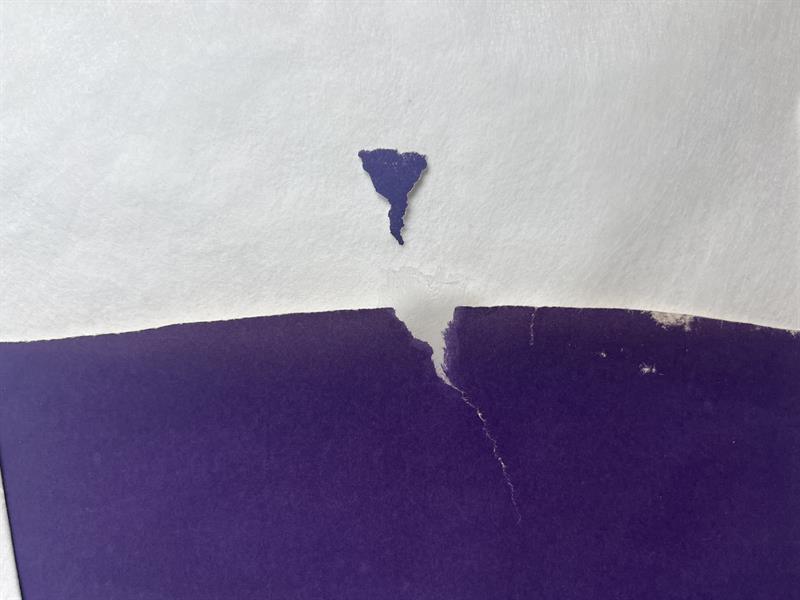 A broken edge of a purple print and the small piece of colored paper that will be used to fill the loss.