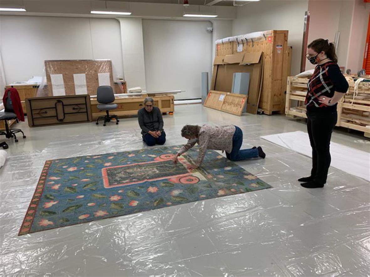 Student and staff members lay a large textile on a sheet of plastic on the floor.