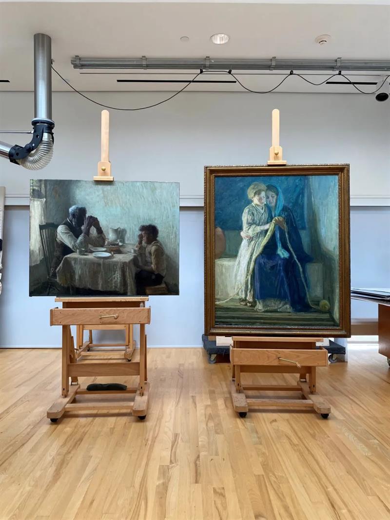 Two paintings displayed on easels in a conservation studio.