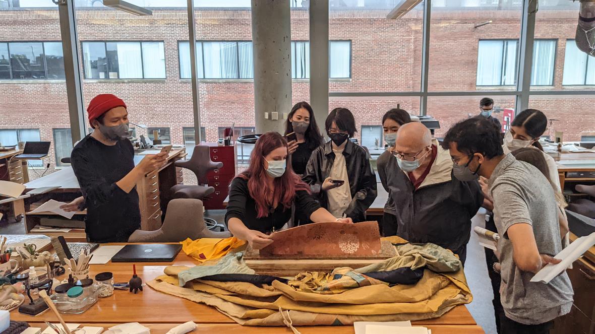 A student lifts the fabric cover to show the object to a tour group.