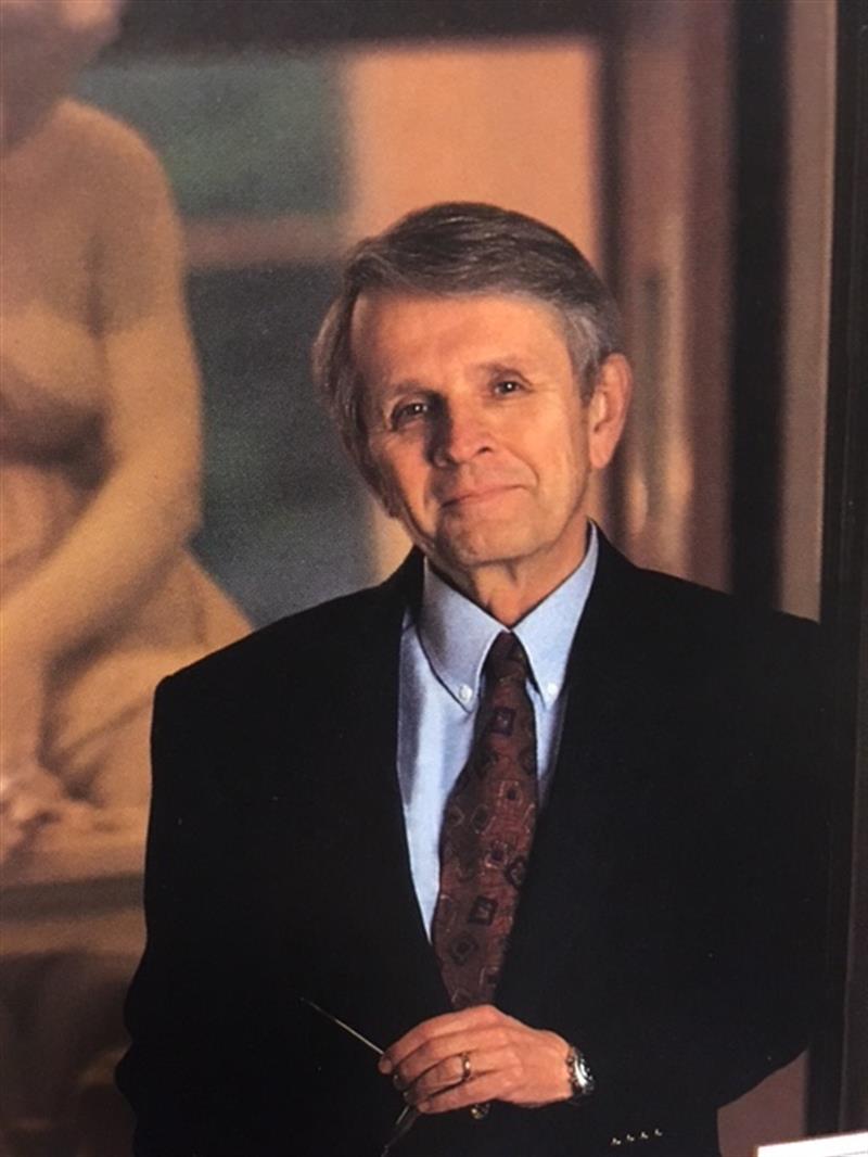 Photo of a man in a suit, standing in front of a painting.