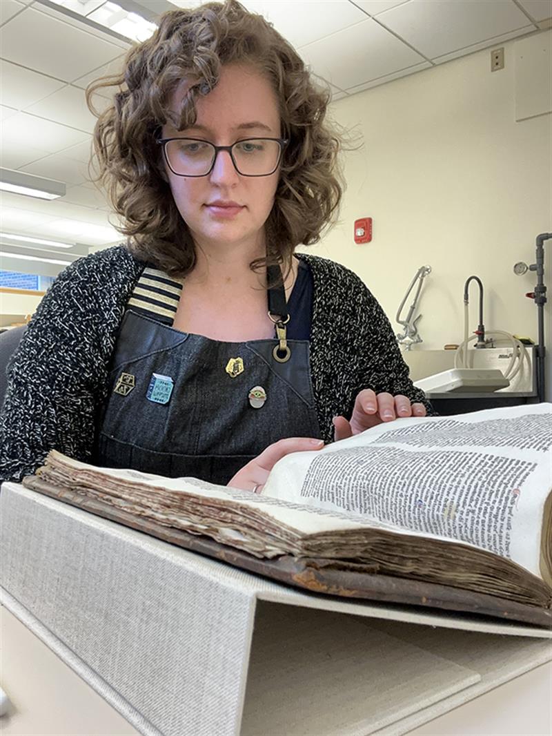 A student examines a book that lays open on a support cradle.
