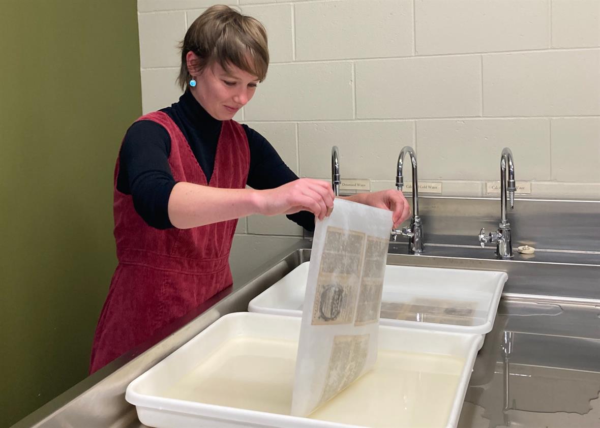 A student lifts a paper and tissue out of a water bath.