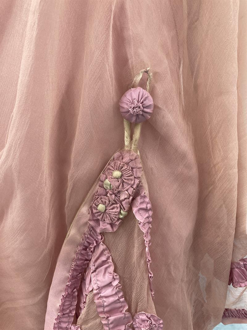 An upholstered button on a pink dress, with the hem of the dress hanging from the button by a loop.