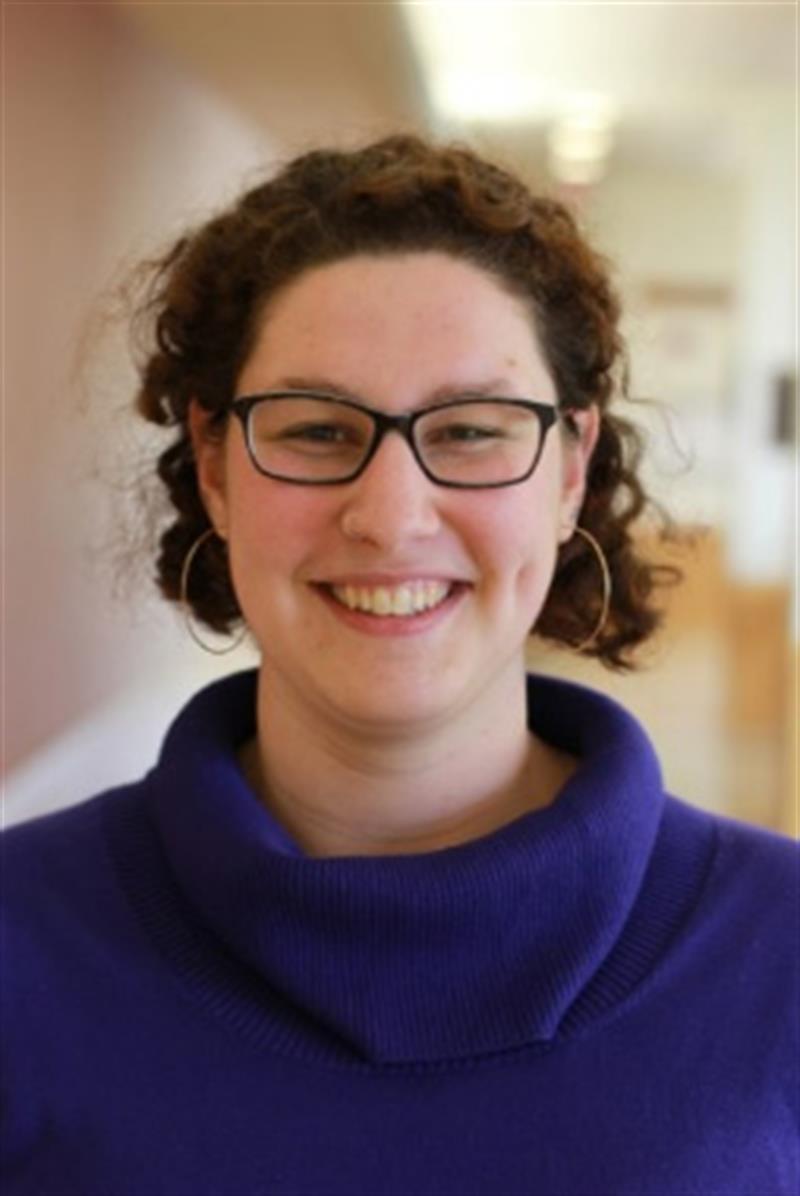 Photo of a woman with short hair, wearing glasses and a purple sweater.