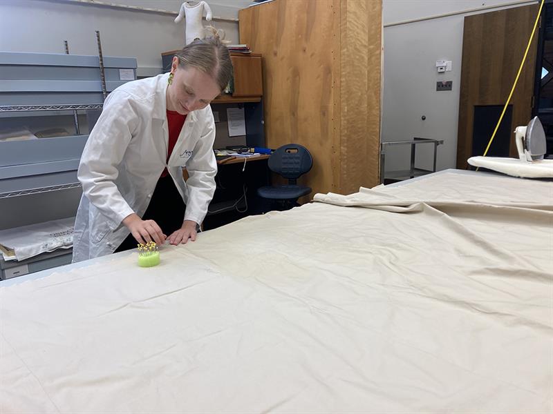 A student in a lab coat places pins along the edge of a piece of fabric.