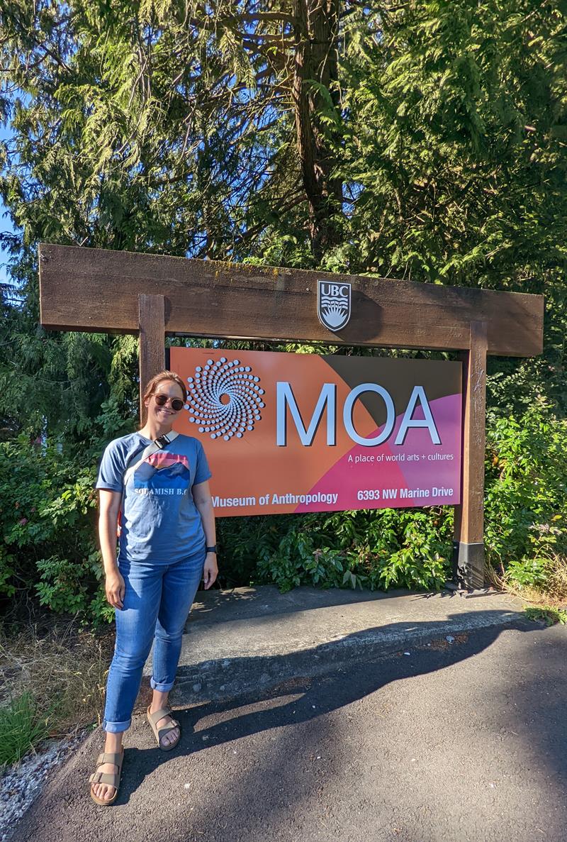 A student, wearing sunglasses, stands outside in front of a museum sign.