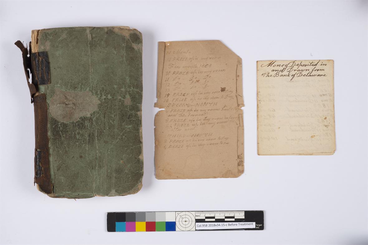 Three parts of the diary laid out on a table: the bound book, a large piece of paper, and a smaller piece of paper.