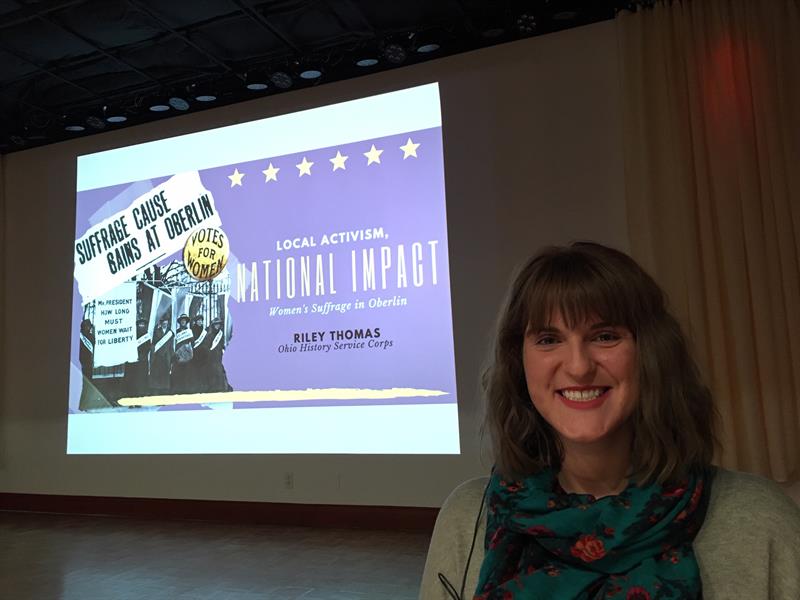 Image of a student standing in front of a projection screen showing a presentation slide for the Women's Suffrage exhibition.