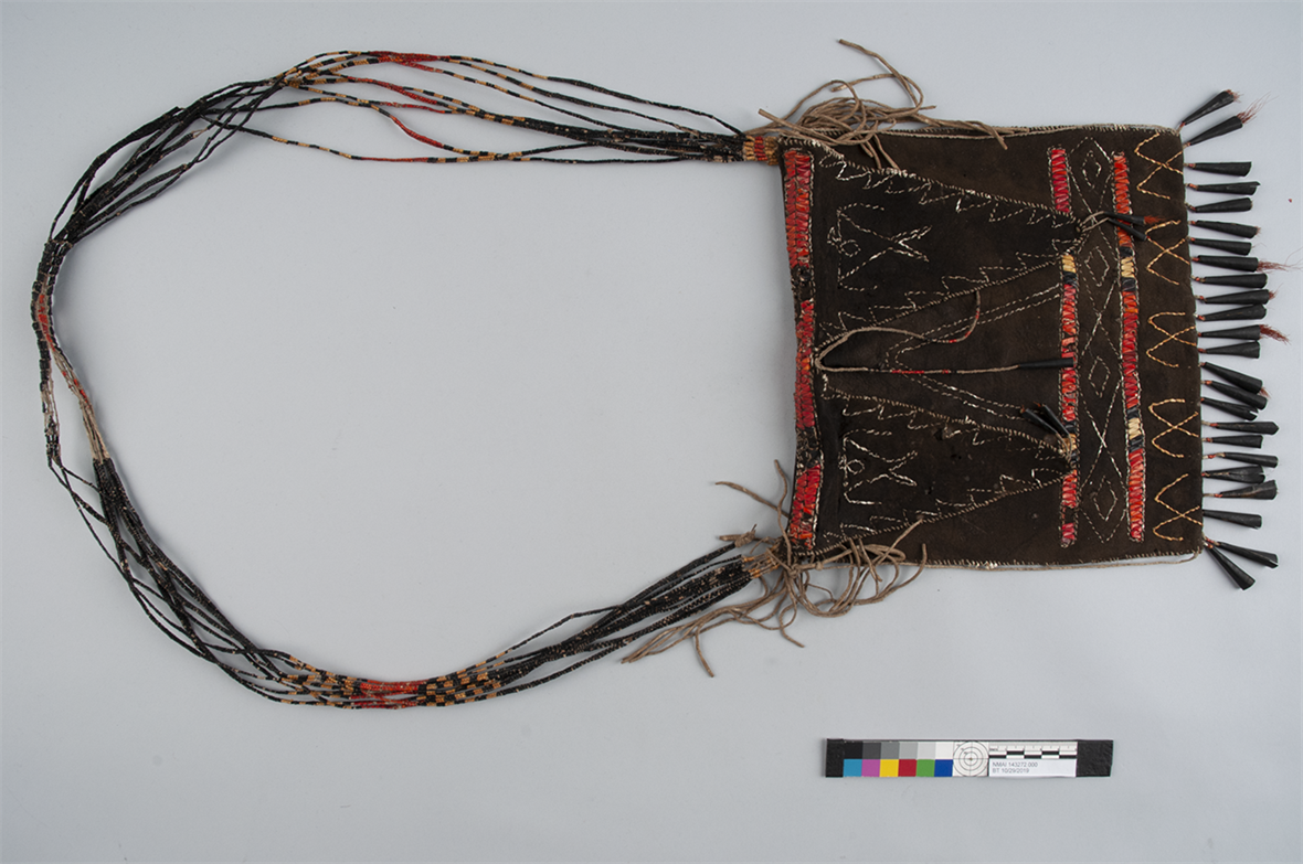 Image of a hide pouch with a woven strap. The pouch is laying on a table. There is a photographic scale and color bar in the lower right coner of the image.