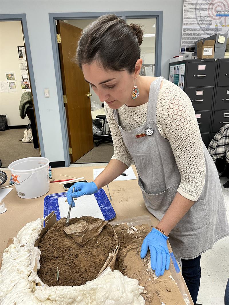 A student brushes away dirt along the inner edge of ah excavated ceramic.