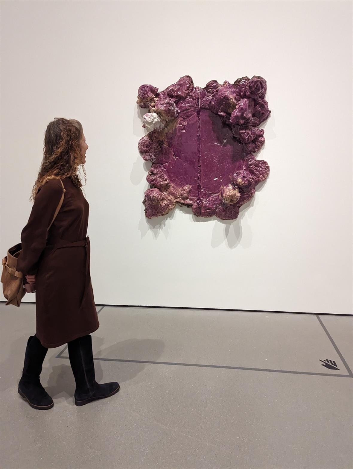 A vistor looks at a purple assemblage art piece on the museum wall.