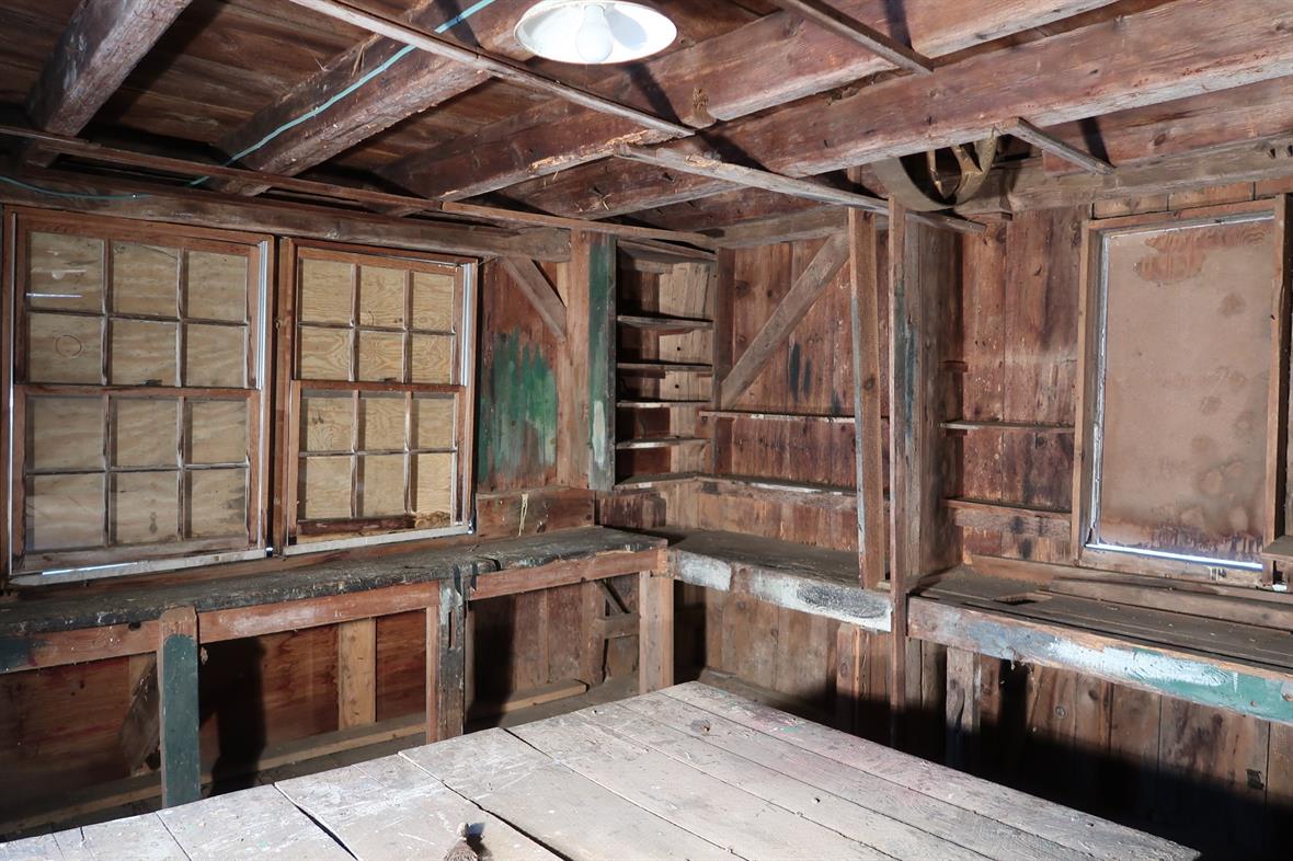 Interior of the wooden structure, with exposed beams and floors and boarded windows.