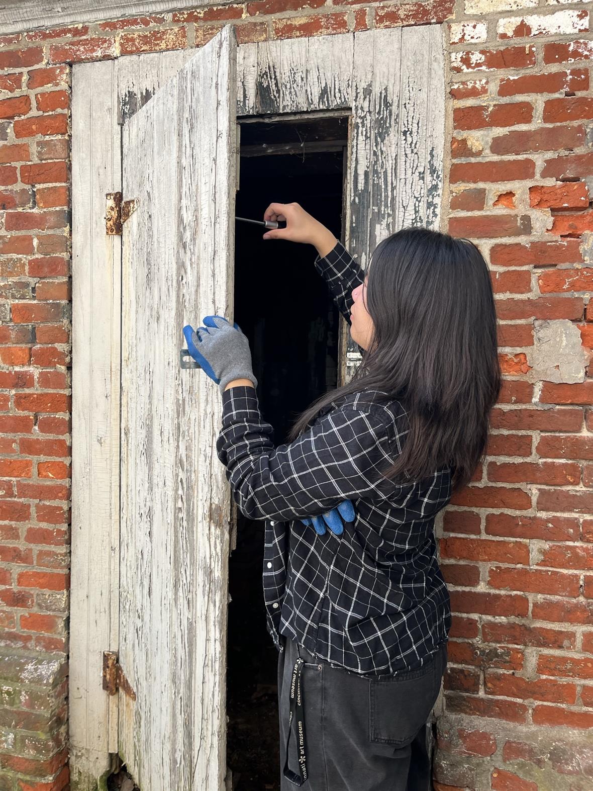 A student uses a screwdriver to fix a door hinge on an historic building.