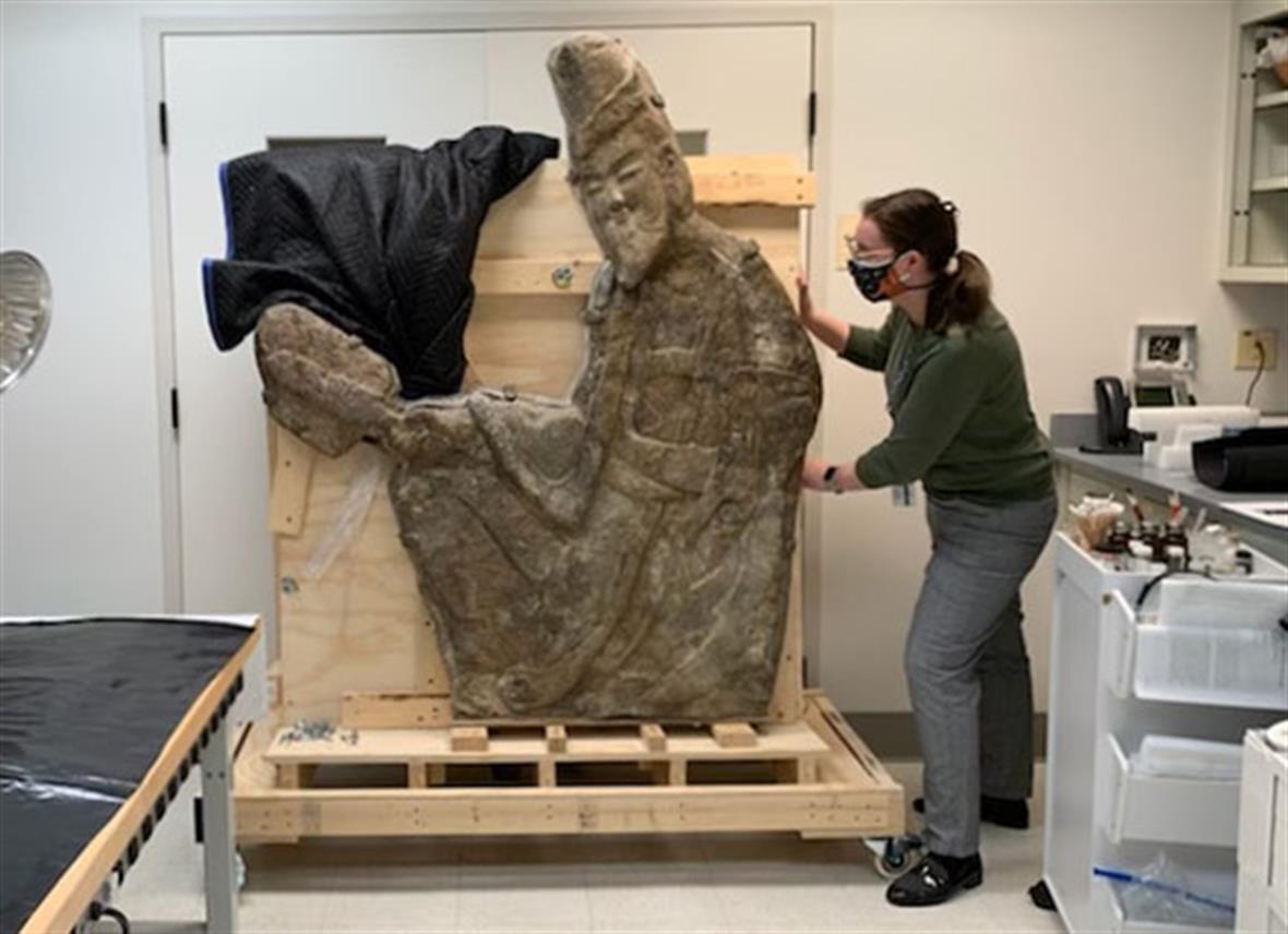 A student makes sure a large stone carving is secure on its storage cart within the lab.