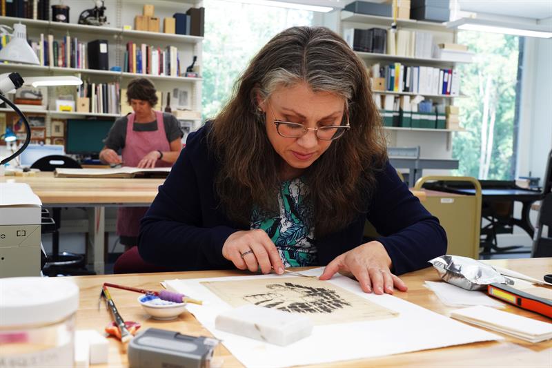 A conservator removing a work on paper from a solid support.