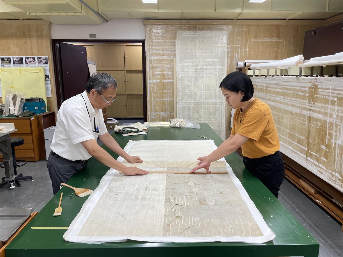 A student and their supervisor investigate the backing material on a delicate silk painting before removing the backing.