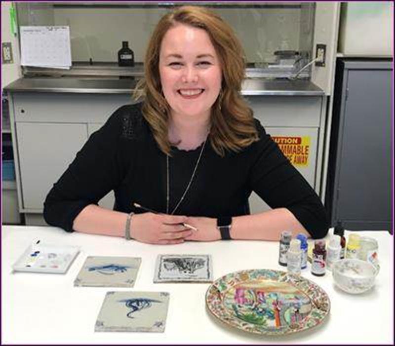 A teacher sits at a table with a selection of ceramic tiles and bowls.