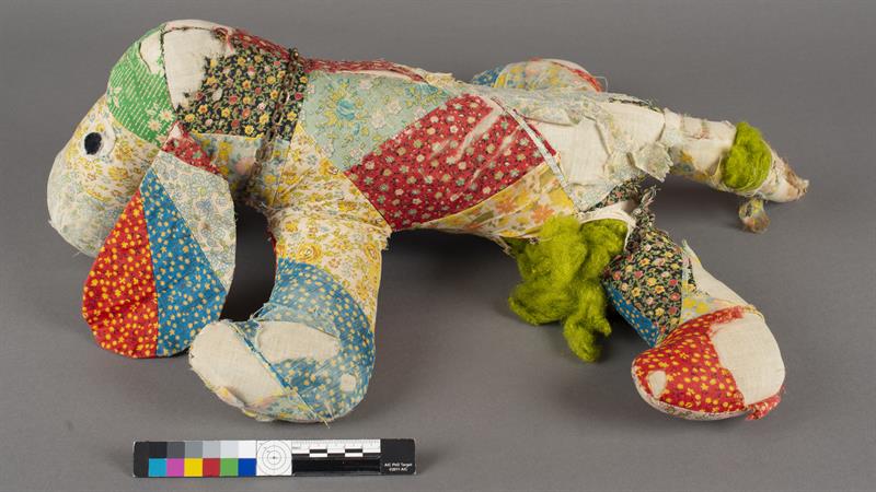 A patchwork stuffed animal, with areas of thinned and broken fabric.